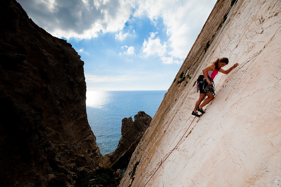 Eine junge Frau, eine Sportkletterin, Freeclimberin, klettert an der Felswand von Ix-Xaqqa, Malta, Sie sichert mit Klemmkeilen, Europa