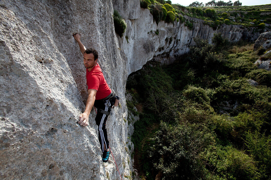 A young man climbing at Mgarr Ix-Xini rocks, Flakeout Walls, Gozo, Malta, Europe