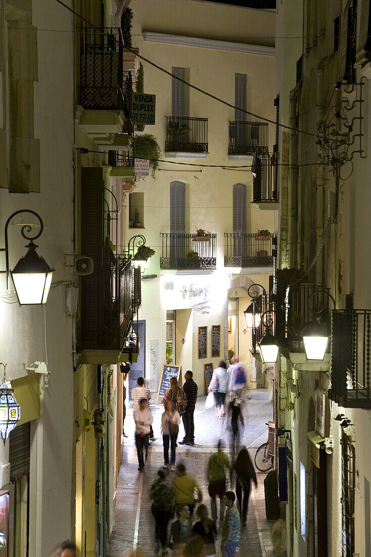 Menschen in einer beleuchteten Gasse bei Nacht, Calle Mayor, Sitges, Katalonien, Spanien, Europa