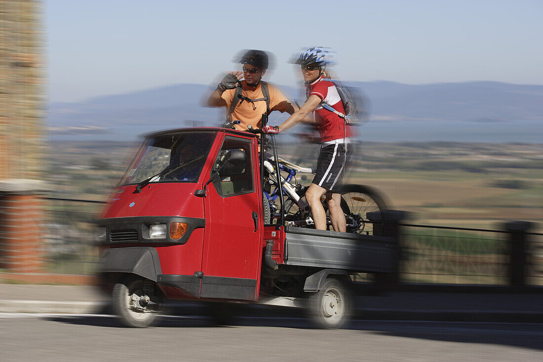 Zwei Mountainbiker auf der Ladefläche eines 3-Rad Transporters in Panicale, Umbrien, Italien, Europa