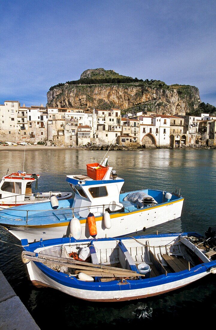 Cefalu, Sicily, Italy  Fishing harbor of the medieval town in late afternoon light  Boats tied to dock  Village and giant rock ´la rocca´ in background  province of Palermo