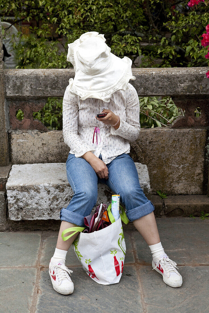 Young Chinese woman with big hat using her mobile phone, Hill of the Sleeping Buddha, Taihua Temple, Kunming, Yunnan, People's Republic of China, Asia