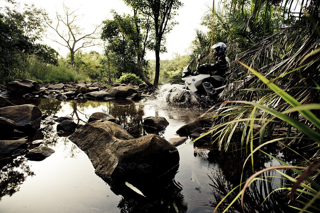 Man on motorcycle driving through a river, Mali, Africa