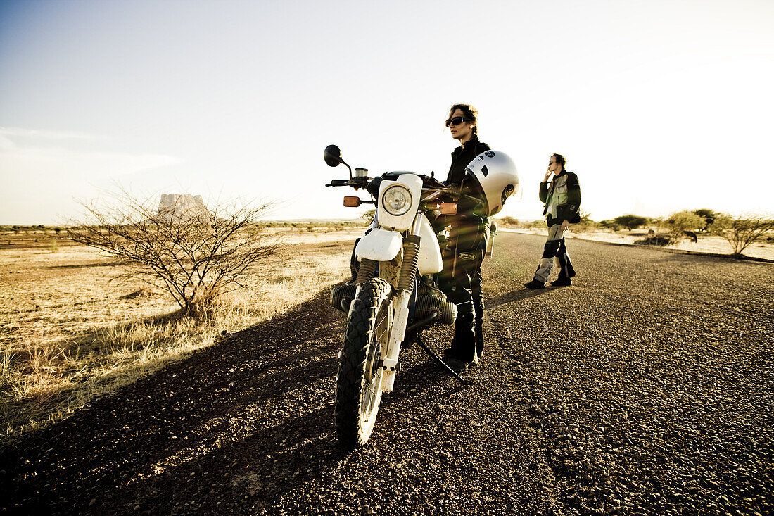 Woman and man with motorcycles on a road in the evening sun, Hombori, Mali, Africa