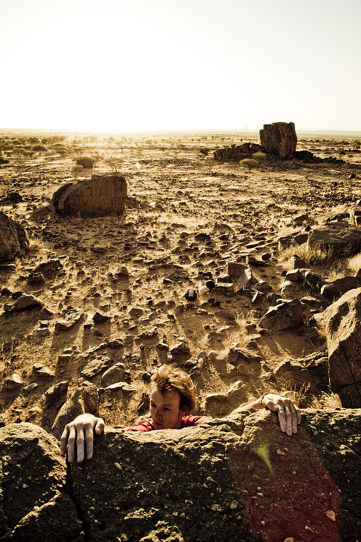 Junger Man klettert an Felskante, Hand der Fatima, Hombori, Mali, Afrika