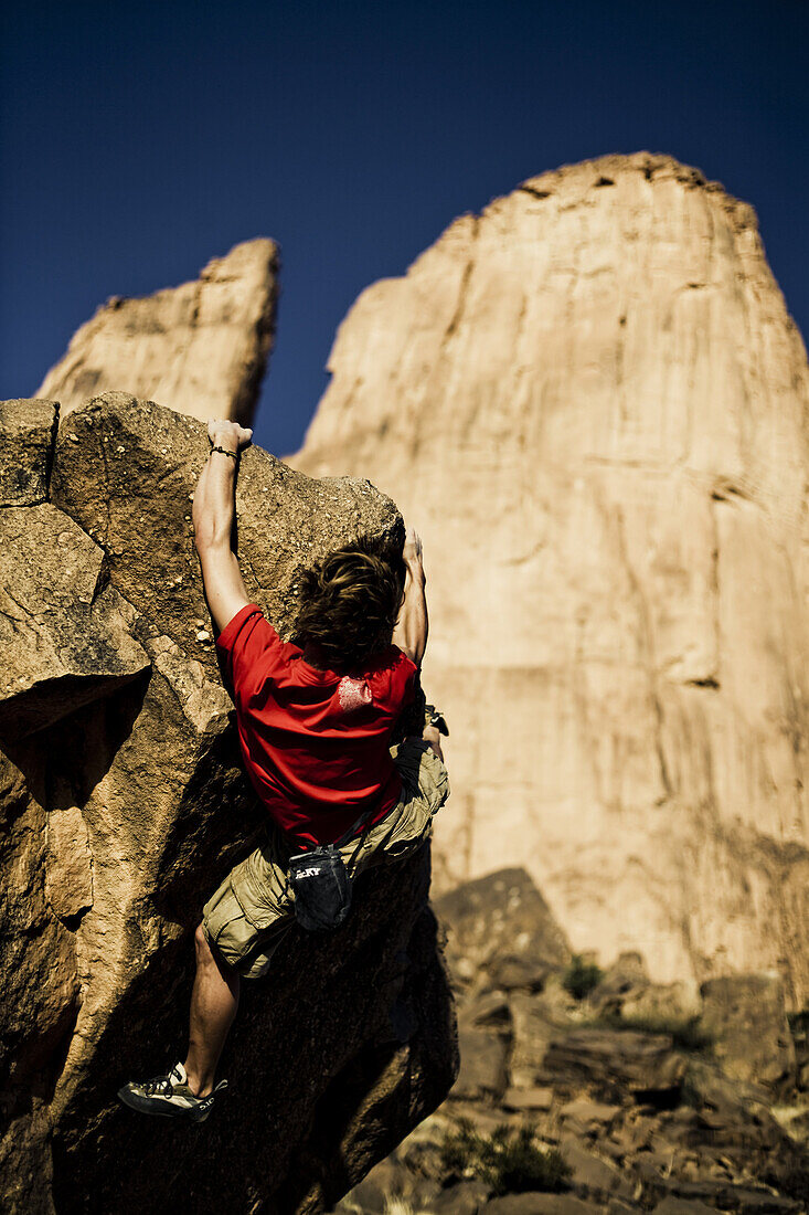 Young man bouldering, Hand of Fatima under blue sky in the background, Hombori, Mali, Africa