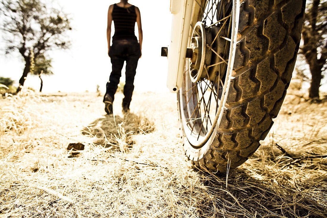 Motorradvorderreifen und Frau im Sonnenlicht, Mali, Afrika