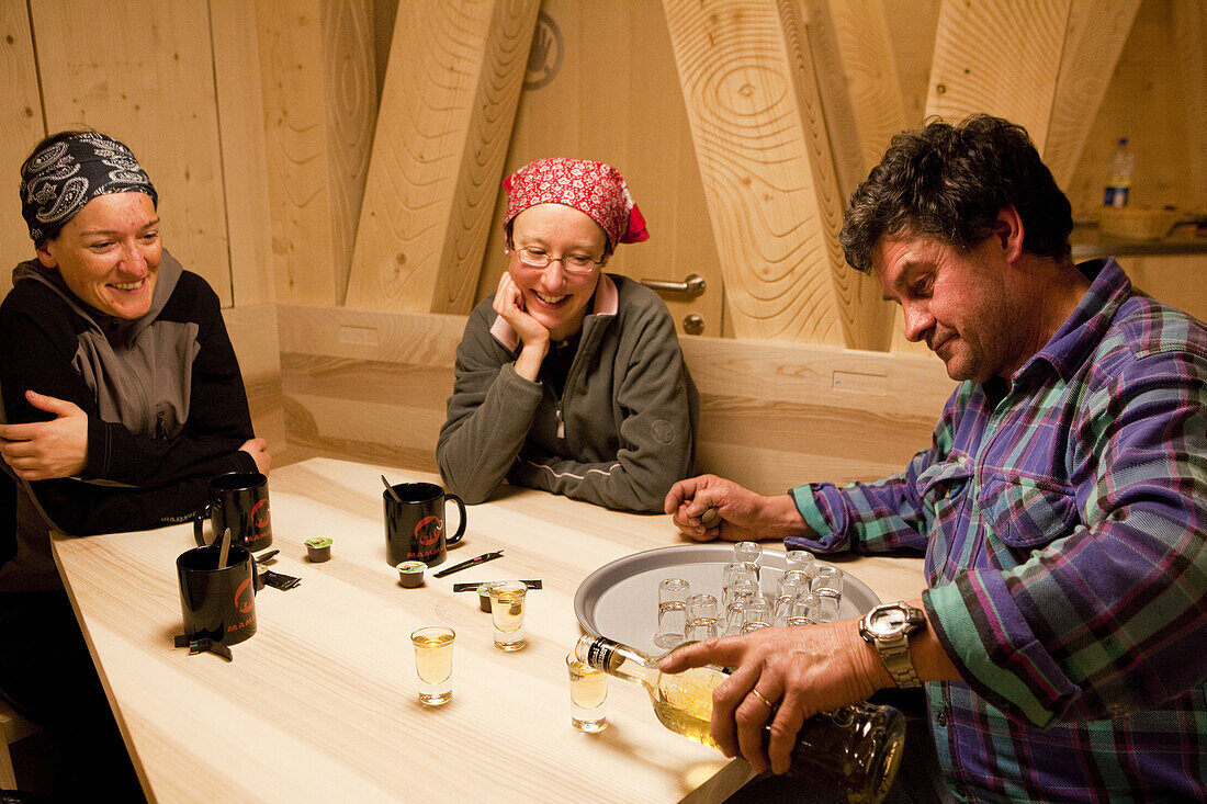 Man pouring herb liqueur into glasses for two women, New Monte Rosa Hut, Zermatt, Canton of Valais, Switzerland