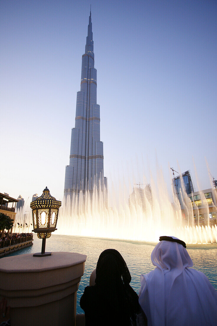 Traditionell gekleidetes Paar an den Wasserspielen am Abend, Dubai Fountain, Burj Khalifa, Burj Chalifa, Dubai, VAE, Vereinigte Arabische Emirate, Vorderasien, Asien