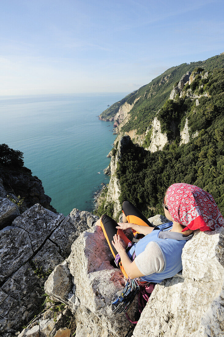 Woman with climbing gear looking towards the steep coast at the Mediterranean, natural park Porto Venere, national park Cinque Terre, UNESCO world heritage site, Liguria, Italy