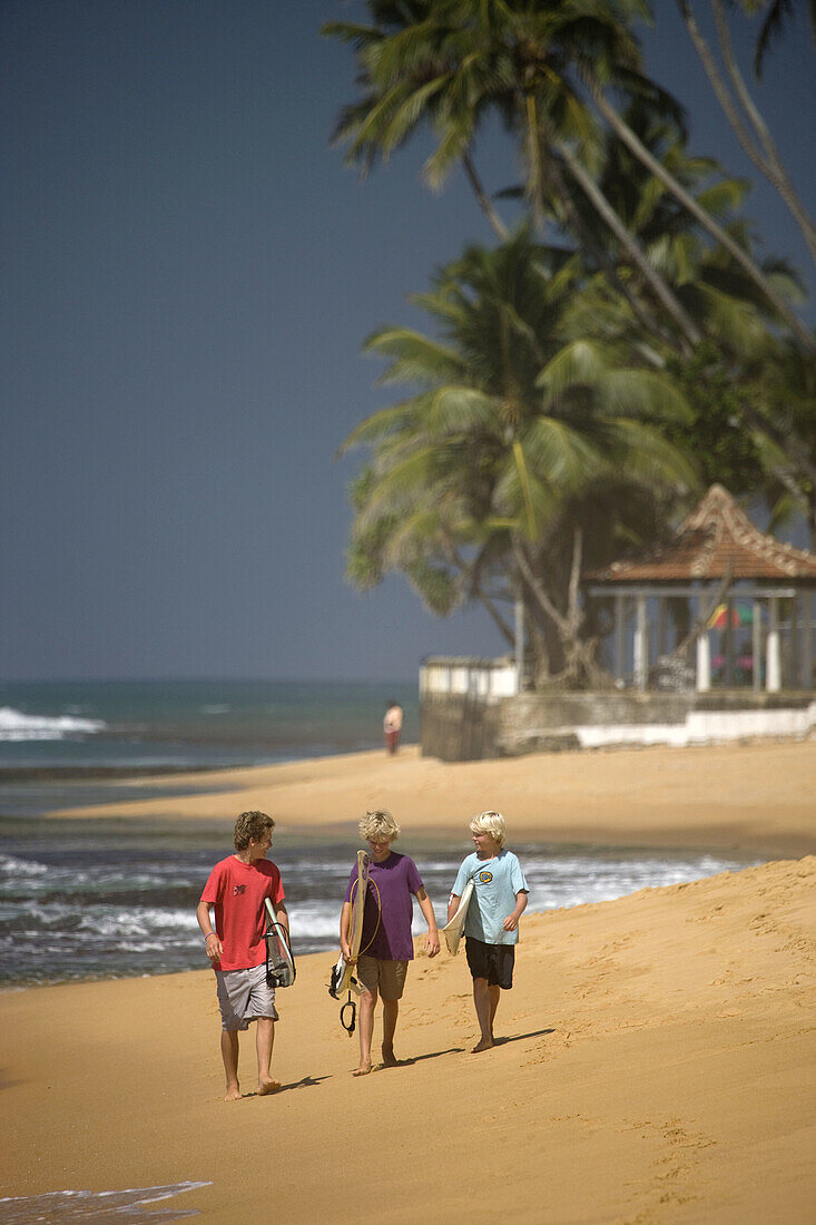 Young surfers walking along Hikkaduwa Beach, Sri Lanka
