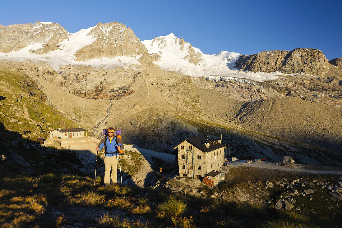 Man hiking, mountain hut Rifugio Chabod and Gran Paradiso in background, Gran Paradiso National Park, Aosta Valley, Italy