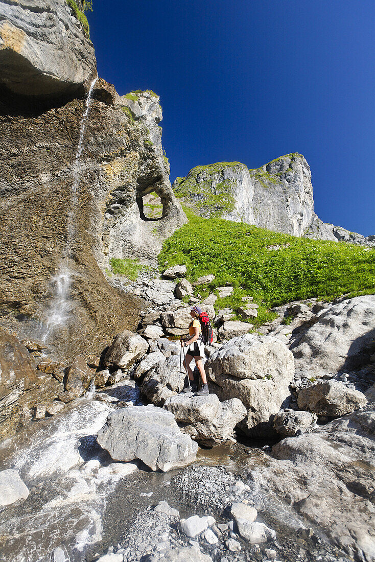 Woman hiking, passing a waterfall, Cirque Fer à Cheval, Haut Giffre, Rhone-Alpes, France