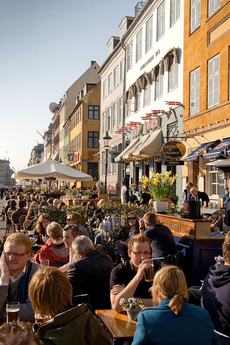 People sitting at waterfront along the Nyhavn Canal, Copenhagen, Denmark