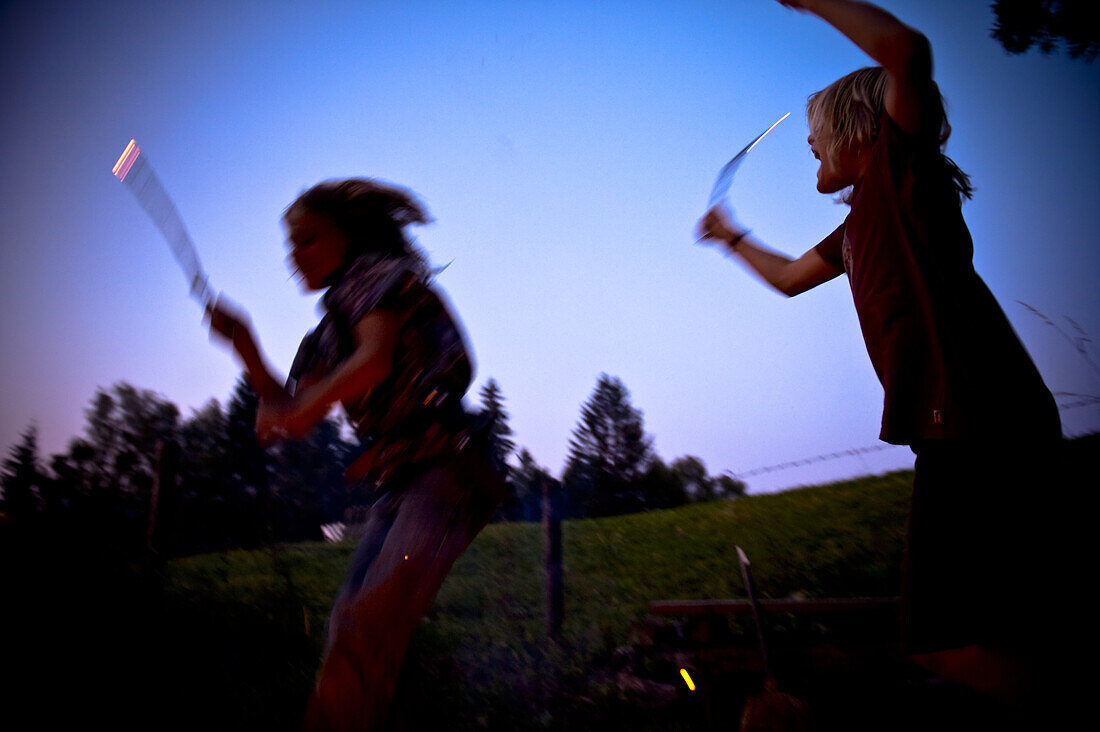 Two boys with glowing wooden sticks in twilight, Austria