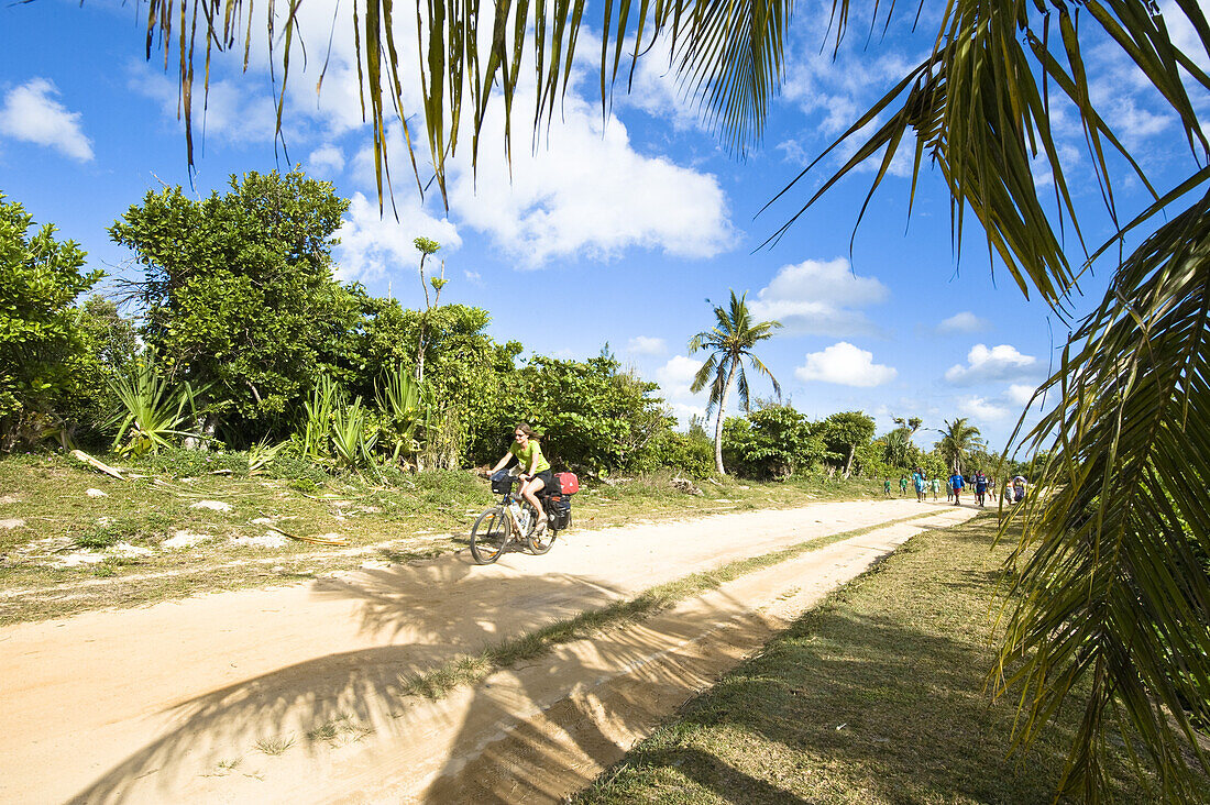Frau fährt mit Fahrrad über Sandpiste zwischen Palmen, Madagaskar
