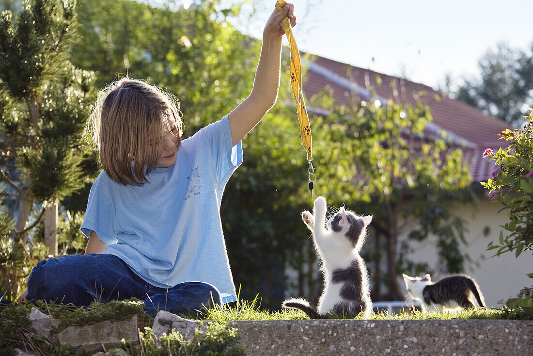 Girl playing with young domestic cat, kitten in the garden, Germany