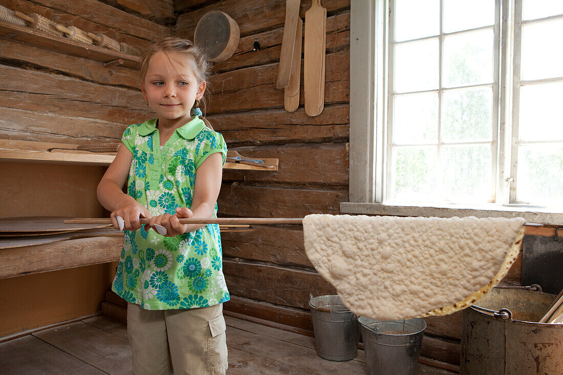 A girl is baking tunnbroed in the open air museum Gammlia, Umea, Vaesterbotten, Sweden, Europe