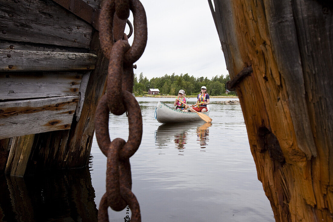 Ein Mädchen und eine Frau in einem Kanu zwischen Schiffswracks, Insel Norrbyskär, Norrbyskär, Västerbotten, Schweden., Europa