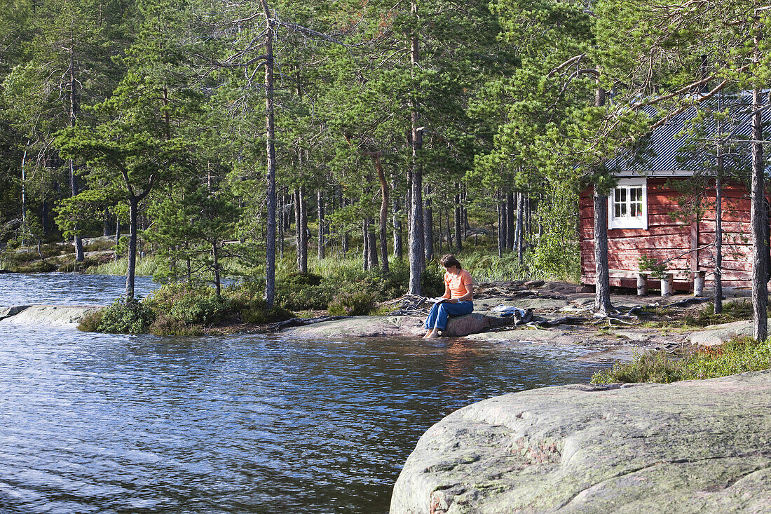 Woman sitting in front of a small cottage at the lake Tärnättvatten, national park Skuleskogen, Höga Kusten, Vaesternorrland, Sweden, Europe
