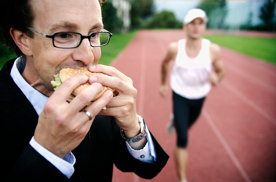 Businessman eating a burger, runner in background