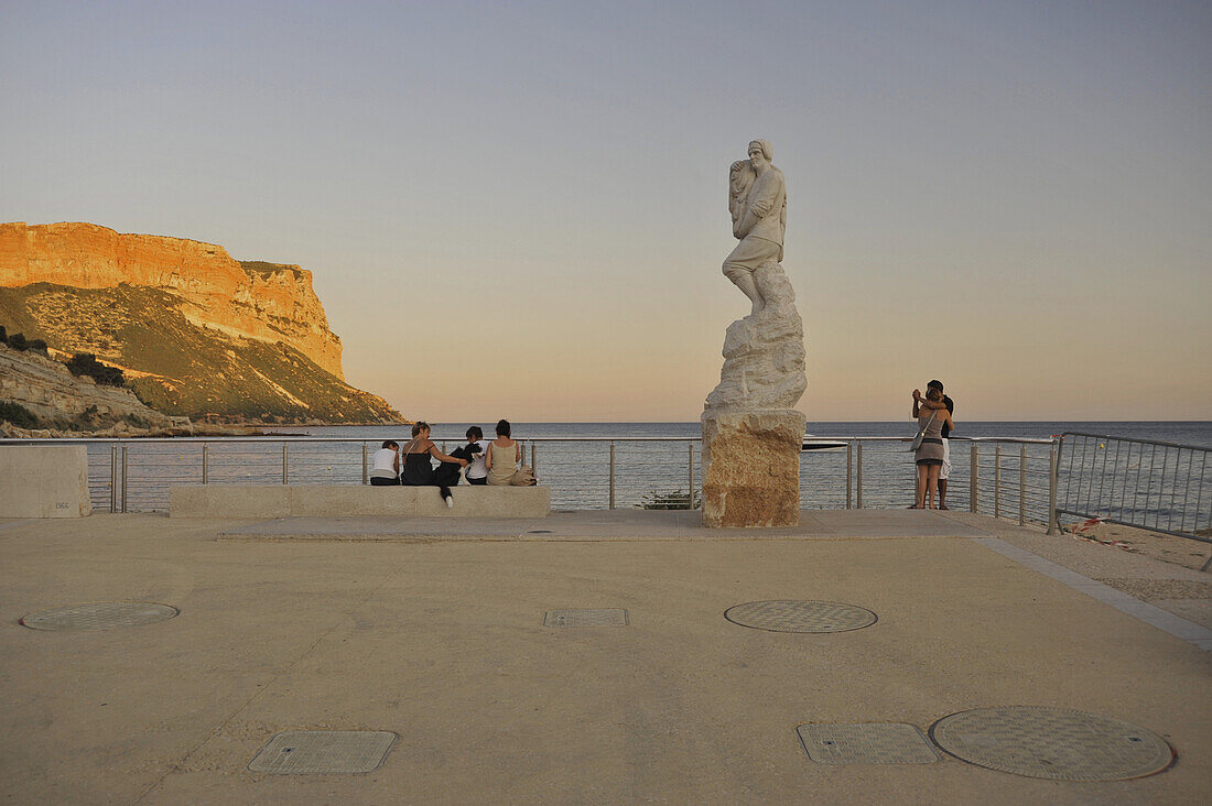 Menschen und Fischerdenkmal an der Promenade und Felsen im Abendlicht, Cassis, Côte d´Azur, Bouches-du-Rhone, Provence, Frankreich, Europa