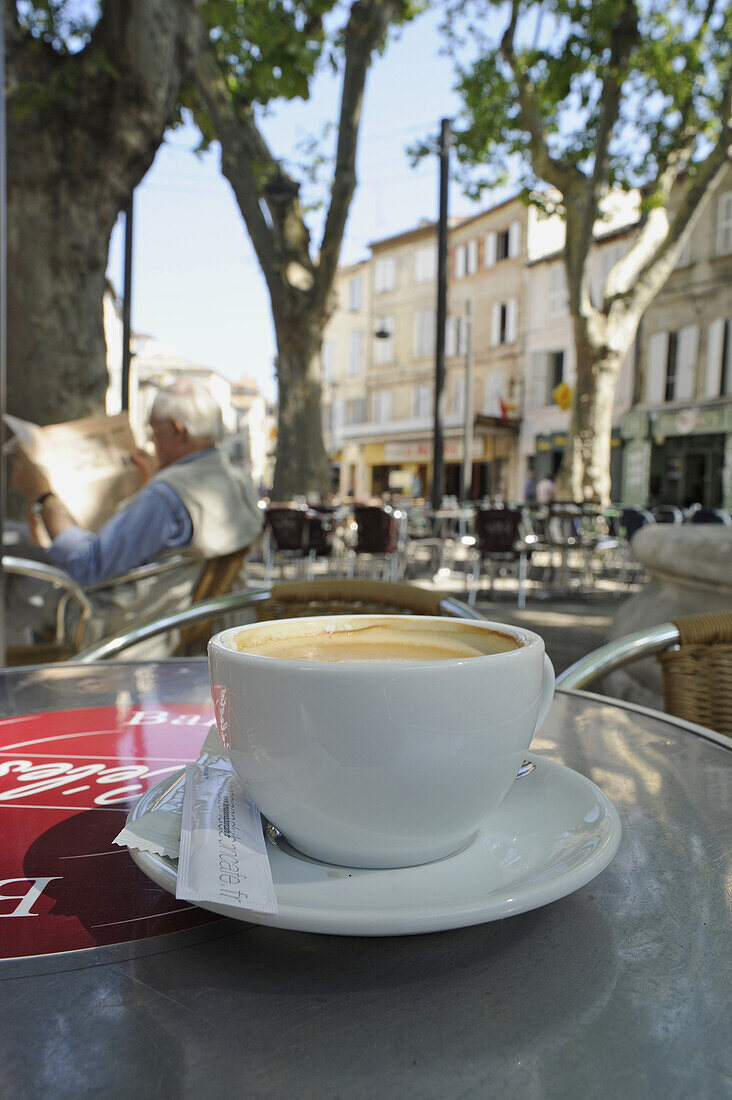 Kaffeetasse und alter Mann mit Zeitung in einem Strassencafe unter Bäumen, Place des Corps Saints, Avignon, Vaucluse, Provence, Frankreich, Europa
