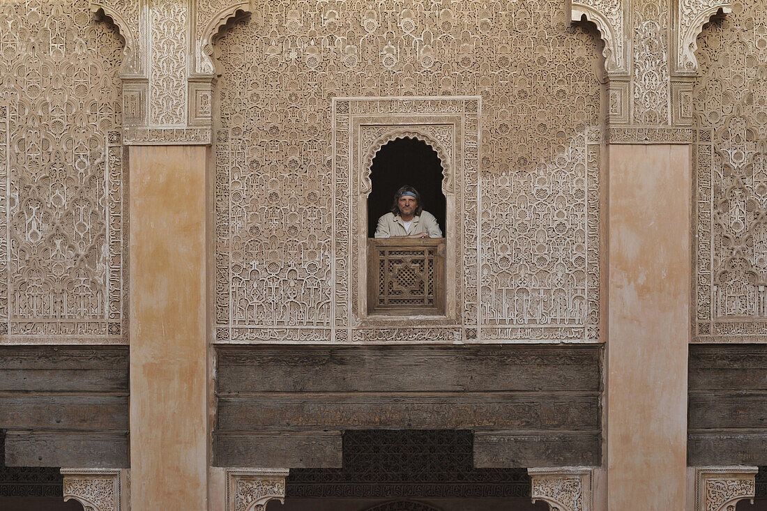 Mann schaut aus Fenster der Medersa Ben Youssef, verzierte Wände im marokkanisch islamischen Stil, Marrakesch, Marokko, Afrika