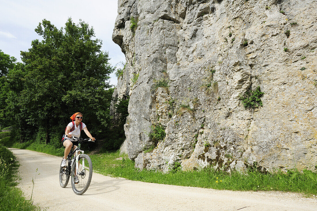 Radfahrerin fährt an Felswand vorbei, Altmühltal-Radweg, Naturpark Altmühltal, Altmühltal, Bayern, Deutschland