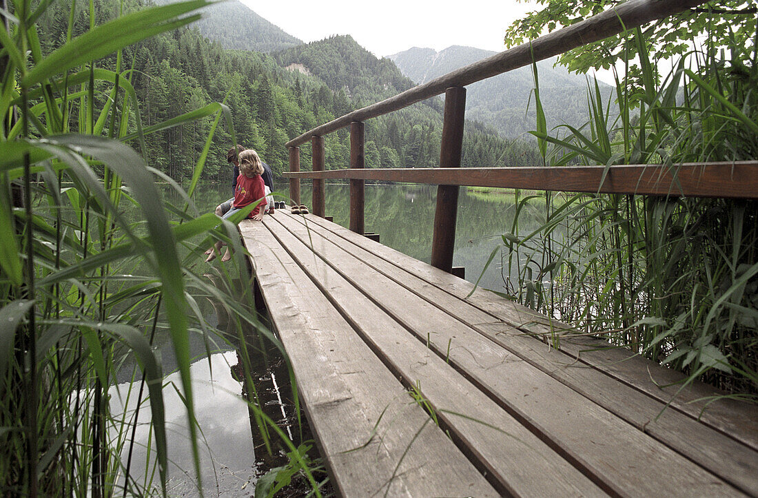 A little girl sitting on a wooden platform at a lake, Schaffner Weiher, Stodertal, Austria, Alps, Europe