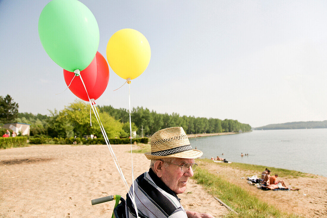 Senior man in a wheelchair with balloons at lake Kulkwitzer See, Leipzig, Saxony, Germany