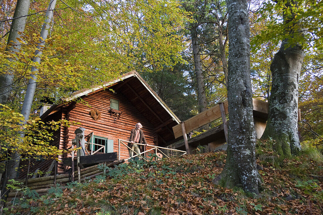 Older man in front of an alpine hut in a deciduous forest, Upper Bavaria, Germany