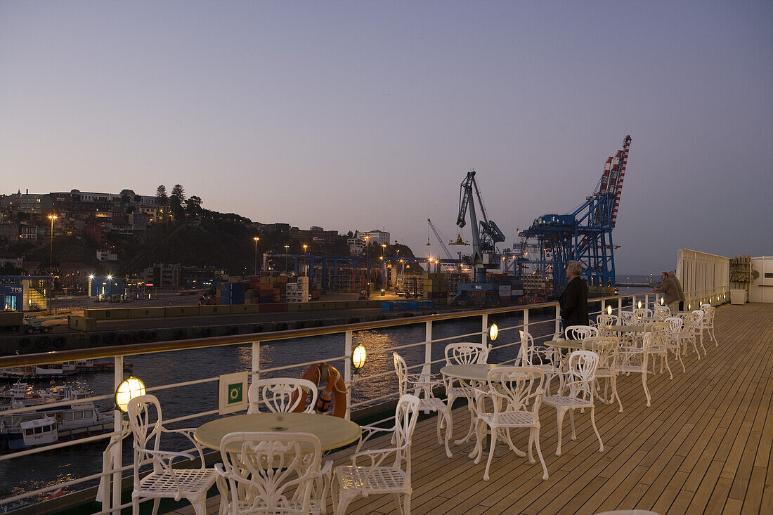 Stühle auf dem Deck von Kreuzfahrtschiff MS Deutschland (Reederei Deilmann) und Lastenkräne im Dämmerlicht, Valparaiso, Chile, Südamerika, Amerika