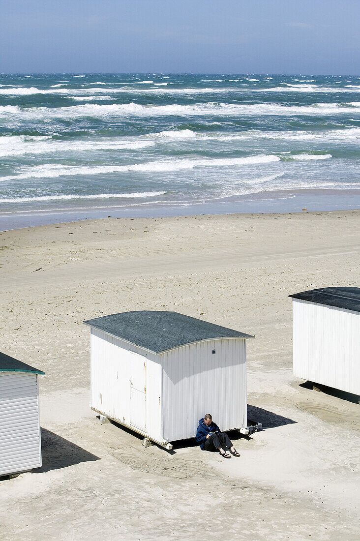 Man reads, leaning on a white bathing huts on the beach, Jutland, Denmark