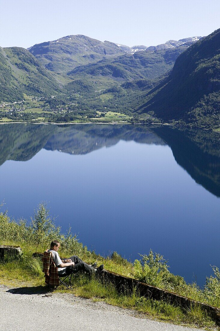 Man reads a book and have a beautiful view over lake and mountains, the Röldals water (Röldalsvattnet), Norway