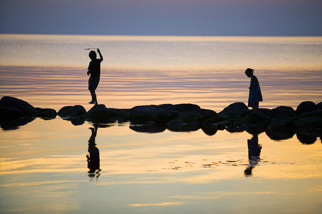 Silhouettes of children playing on a stonewall in the sea