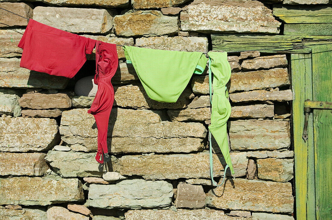 Red and green bikini hangs out to dry on stone hut
