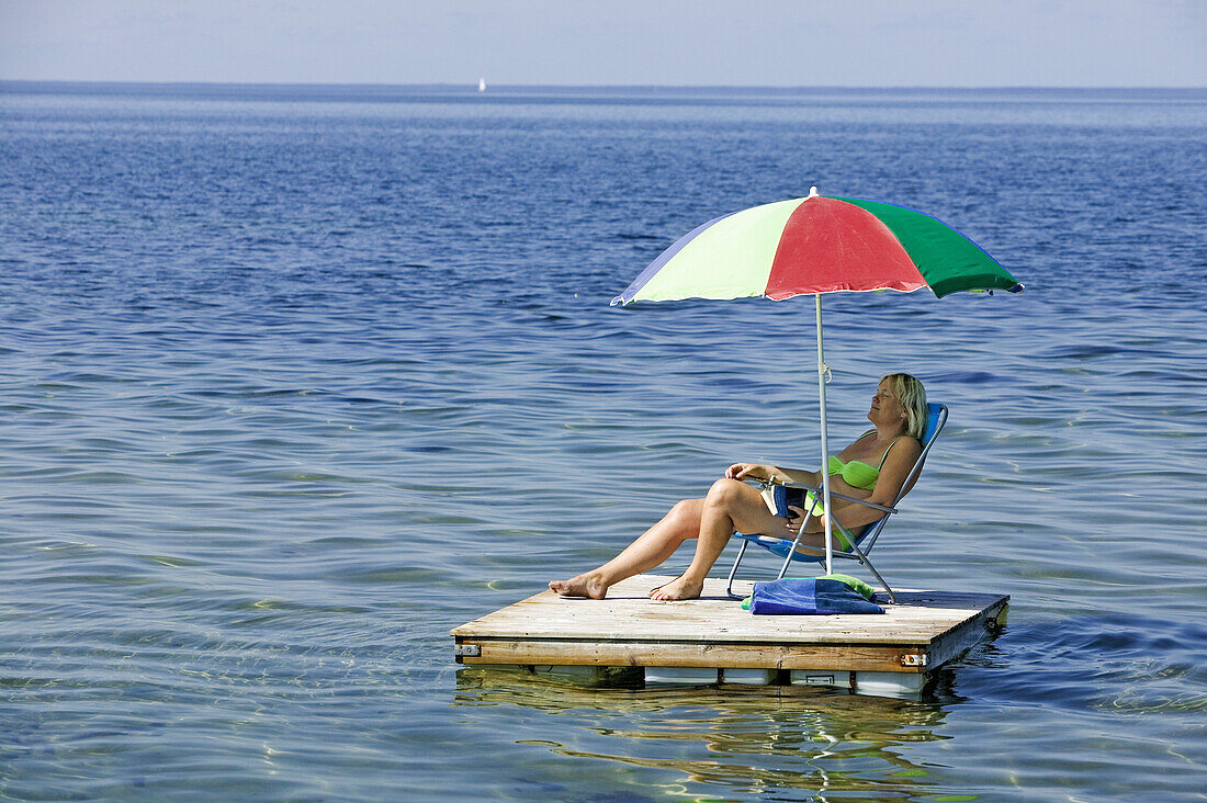 Woman on a raft sitting under a brightly-coloured umbrella