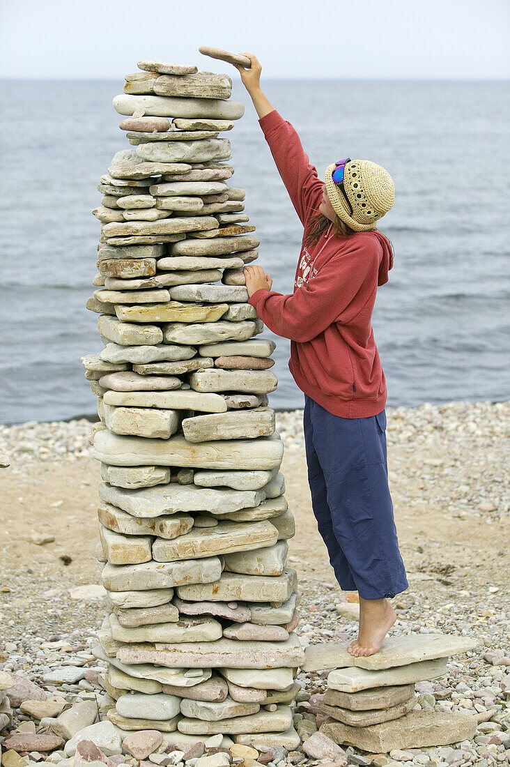 Girl in straw hat and sunglasses is building a stone tower