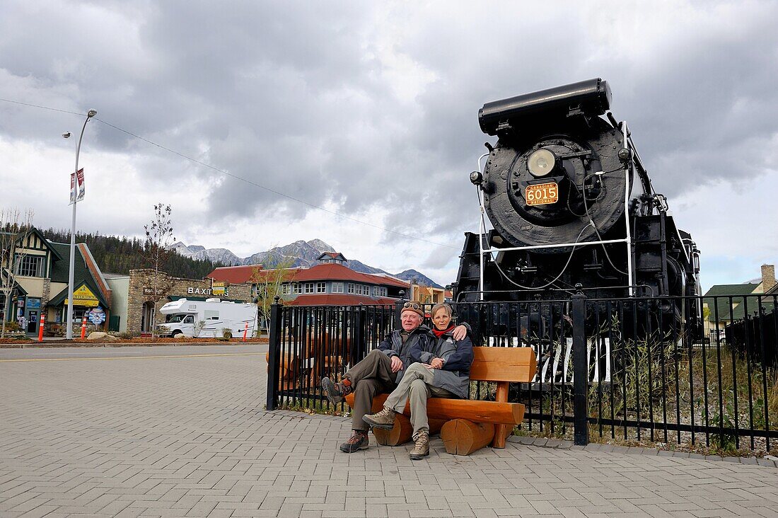 Tourists sitting in front of the historic steam locomotive, town of Jasper, Jasper National Park, Rocky Mountains, Alberta, Canada