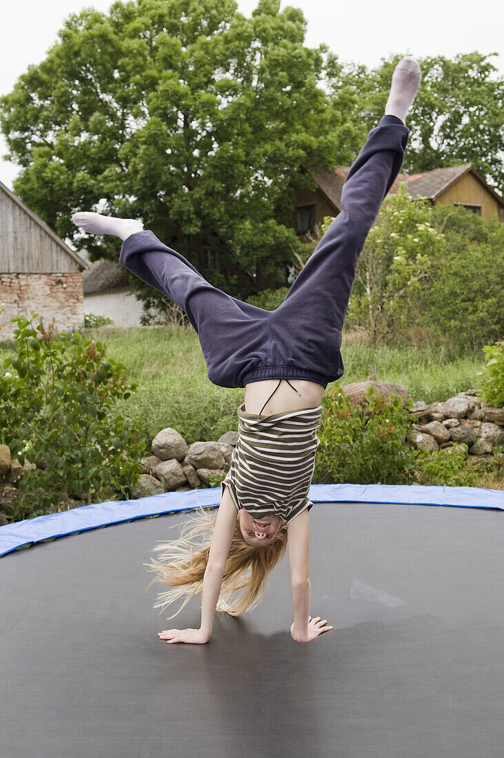 Girl standing on her hands on a trampolin.