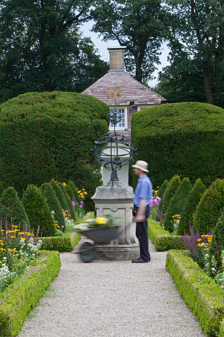Gardener pushing a wheelbarrow in the castle gardens, trimmed hedges in the castle grounds of Clemenswerth Castle in Sögel, Lower Saxony, northern Germany