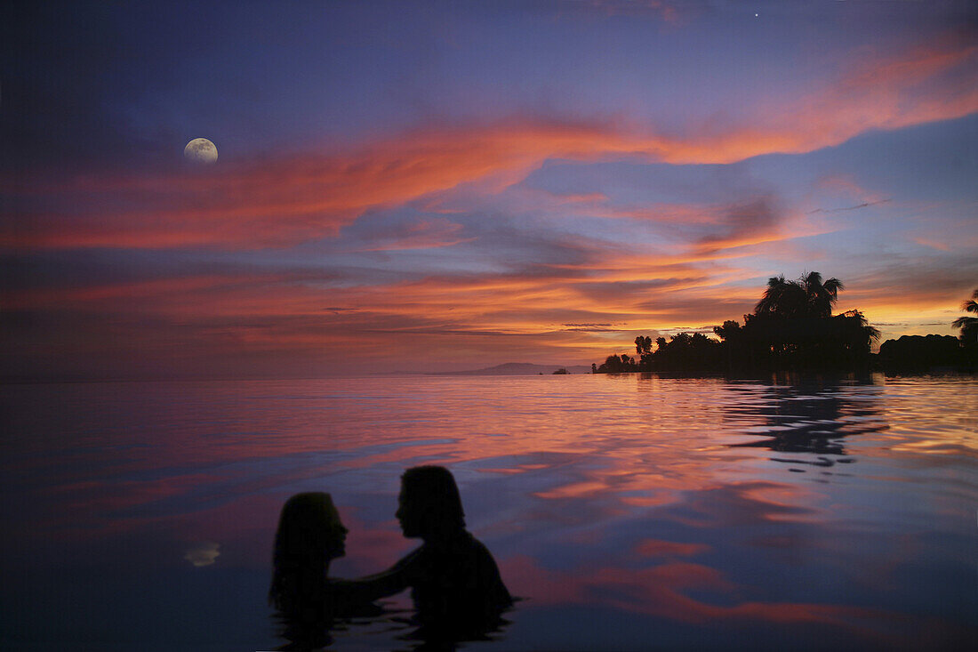 Ein Paar in einem Infinity Pool bei Sonnenuntergang, Bohol Insel, Philippinen, Asien