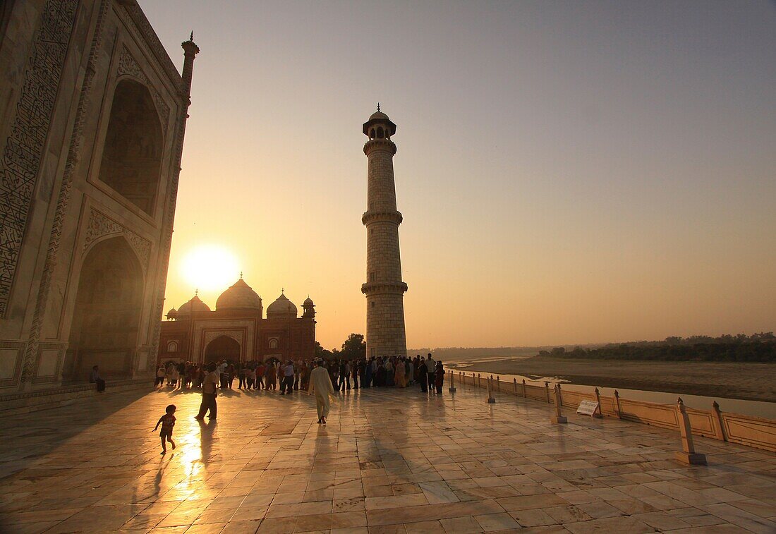 Tourists wait in line on the marble floor to enter the inside of the Taj Mahal, Agra, India as the sun sets over the western mosque