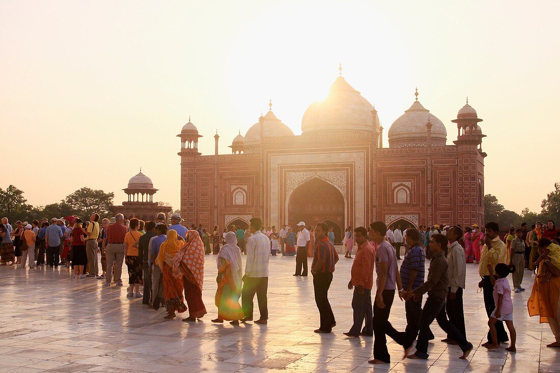 The sun sets over the western Mosque as tourists wait in line on the marble floor to enter to inside of the Taj Mahal, Agra, India