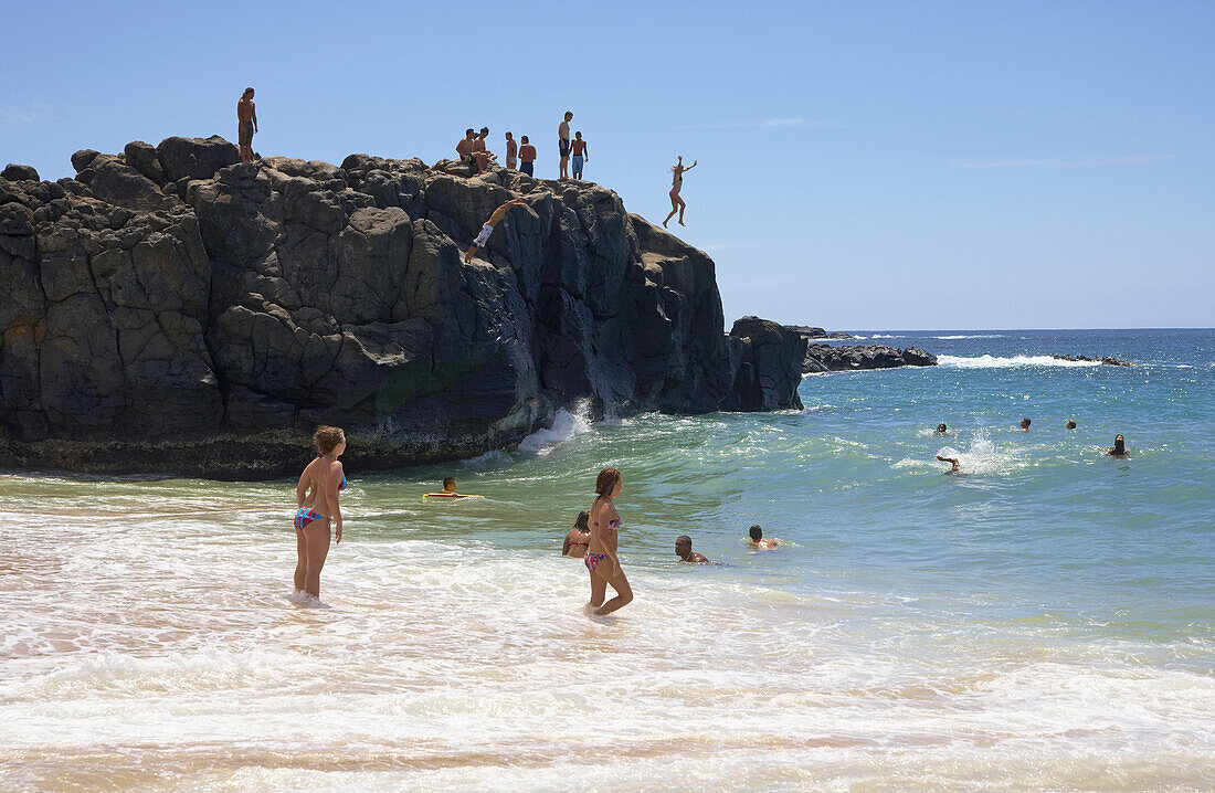 Menschen auf einem Felsen im Meer am Weimea Bay Beach Park, North Shore, Oahu, Hawaii, USA, Amerika