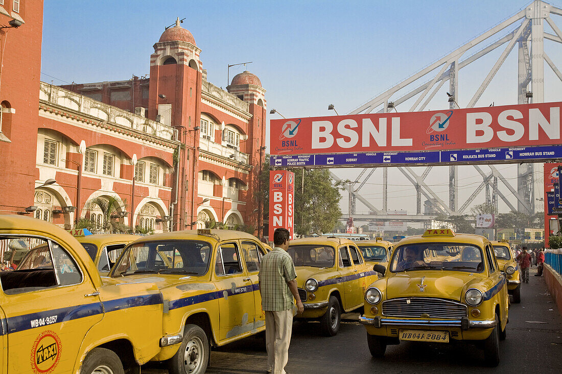 Yellow ambassador taxis outside Howrah train station with Howrah bridge in background, Kolkata, West Bengal, India