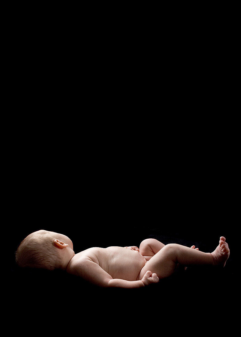Newborn baby lying on a black background with her face turned away from the camera