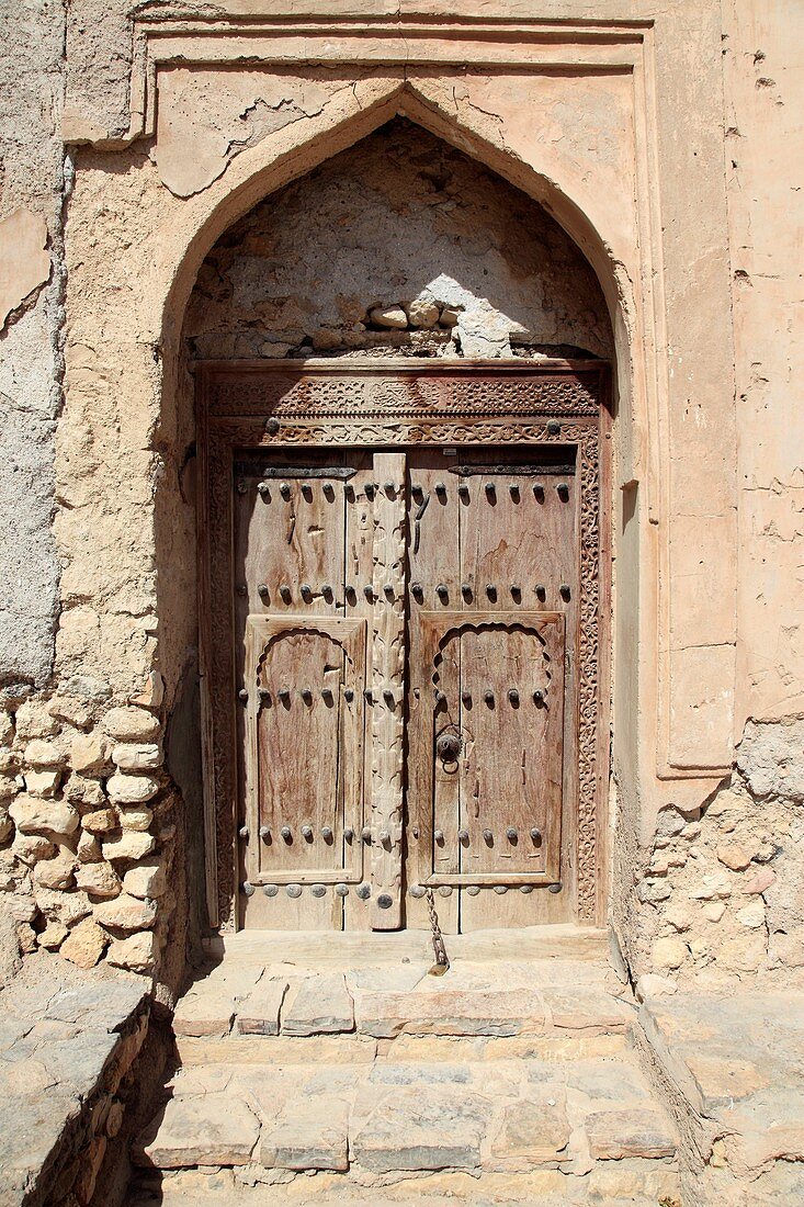 old wooden door in front of the facade of Fort Quriat in the village Quriat, Sultanate of Oman, Asia.