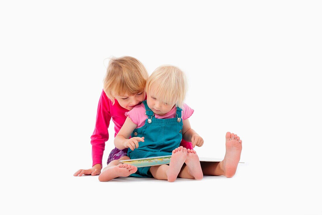 sisters looking at chidren's book - isolated on white